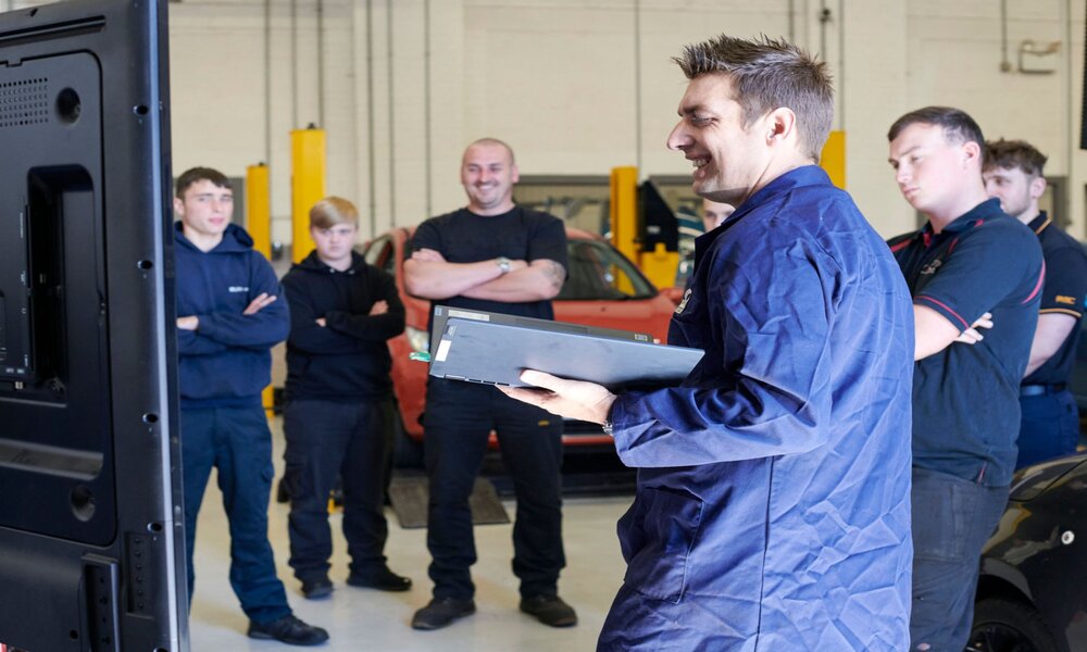 An S&B Academy teacher showing MOT qualification students a car part