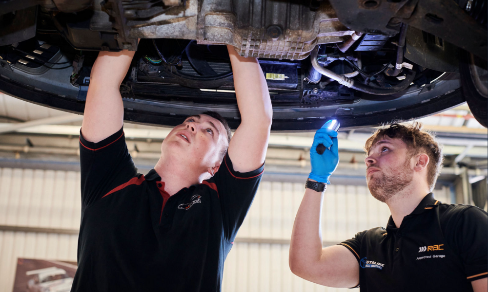 two young automotive technicians examining the underside of a car