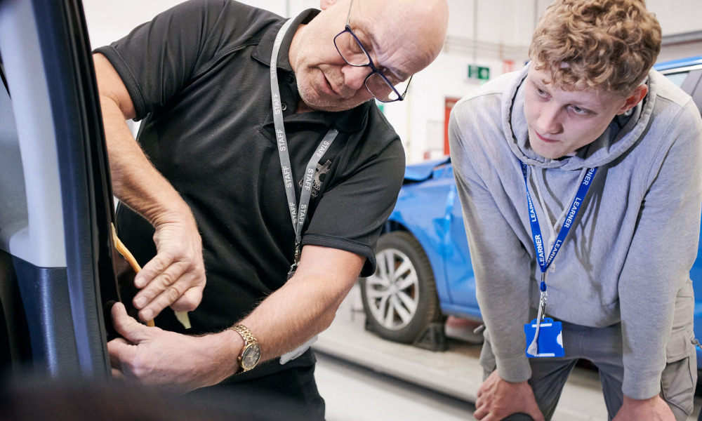 A member of the S&B Academy teaching team showing an automotive apprentice part of a car door